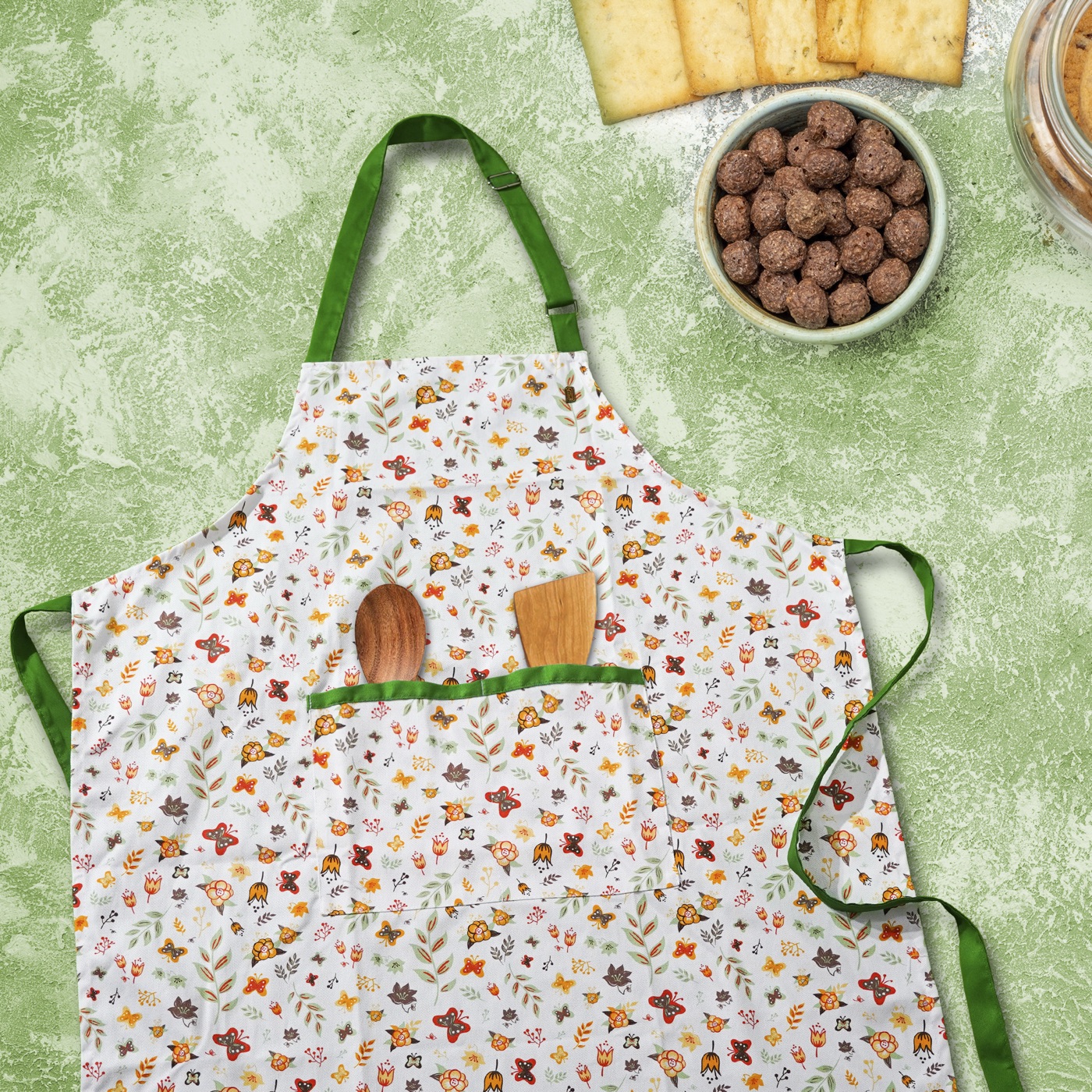 Green-trimmed floral apron laid out with wooden utensils and ingredients