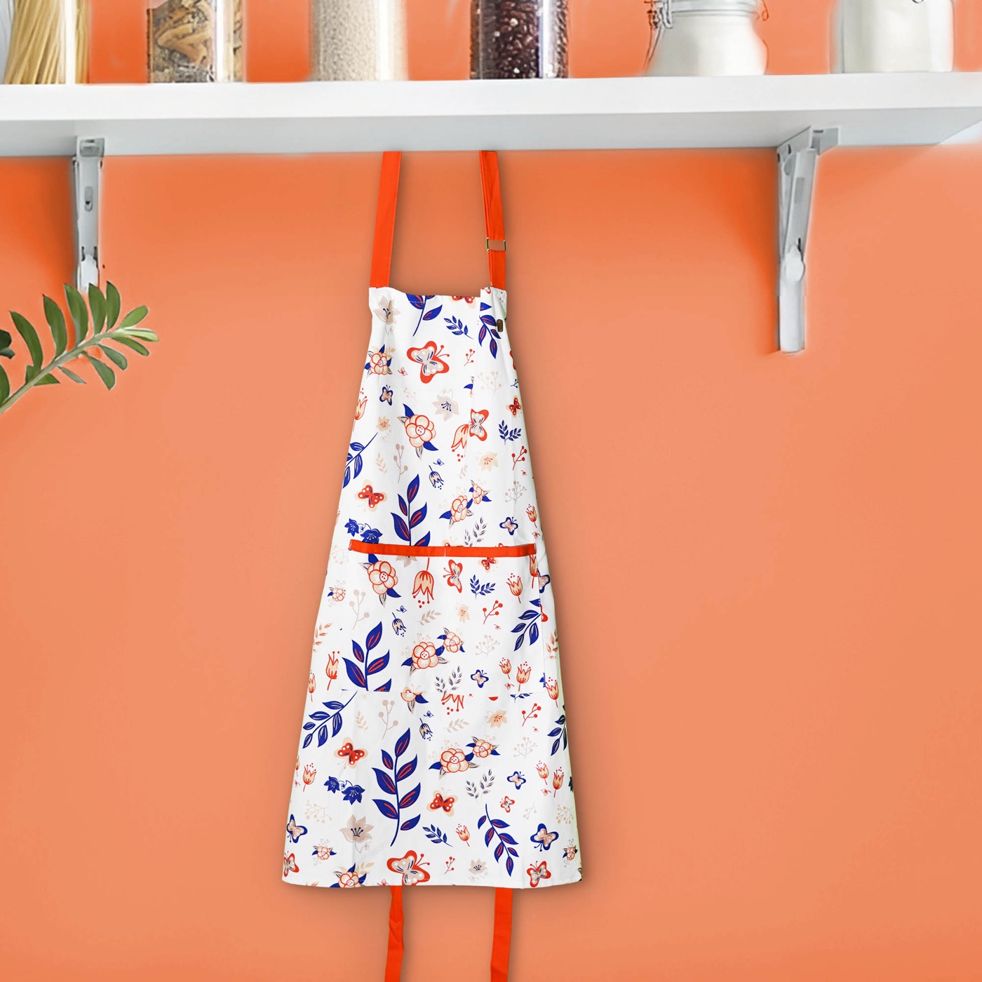 Orange-trimmed floral apron hanging beneath a kitchen shelf