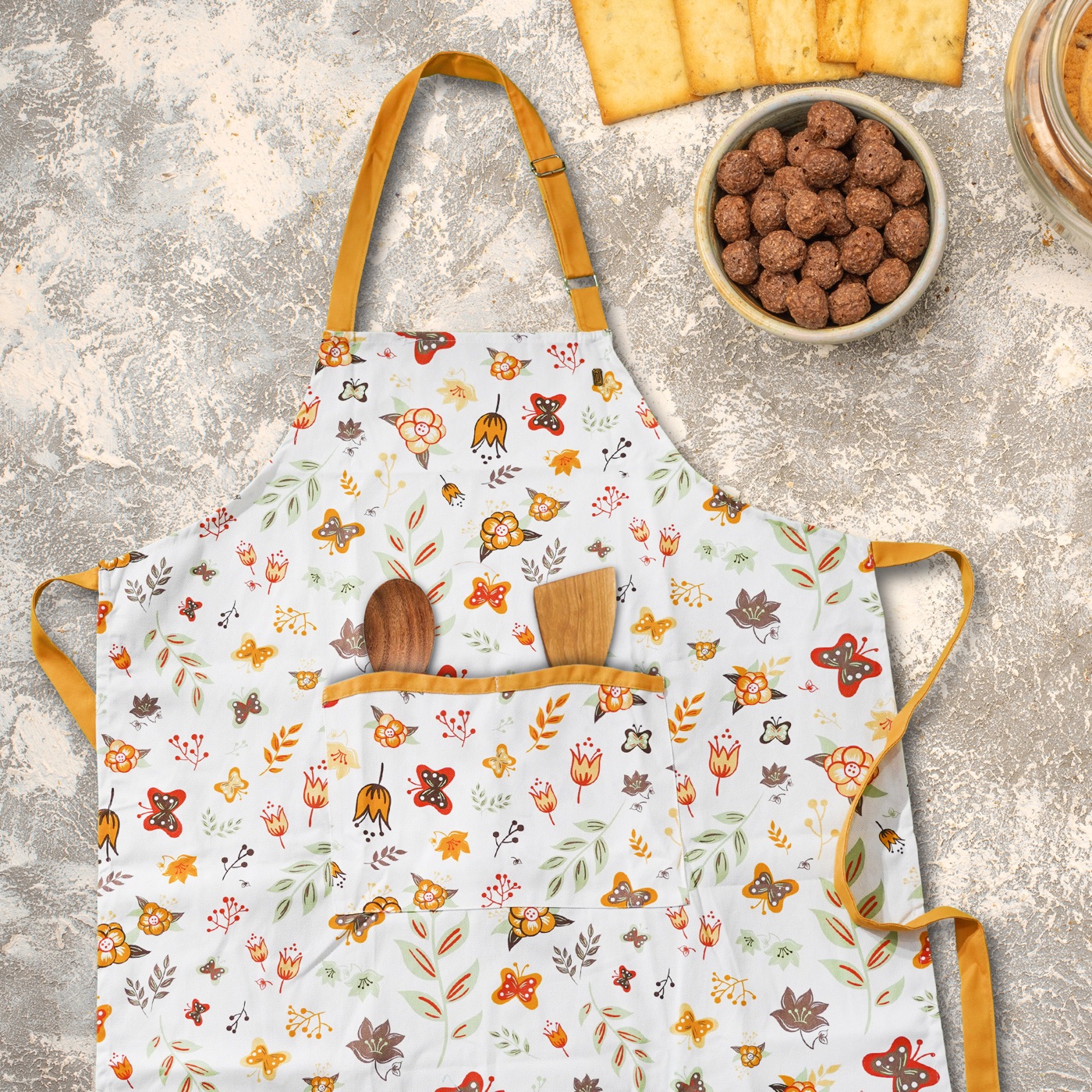 Yellow-trimmed floral apron laid out with wooden utensils and ingredients